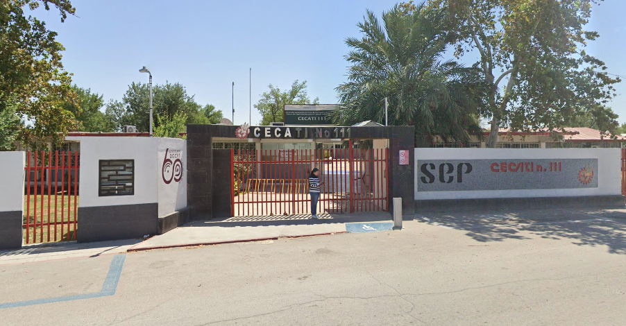 Fotografía en la que se muestra la entrada del plantel, conformada por una reja de acceso color rojo y un arco de color café, en la parte superior del arco hay unas letras que dicen CECATI NÚMERO 111.